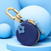 A purple coin purse keychain with a gold clasp and blue fabric, resting on light blue spherical props.