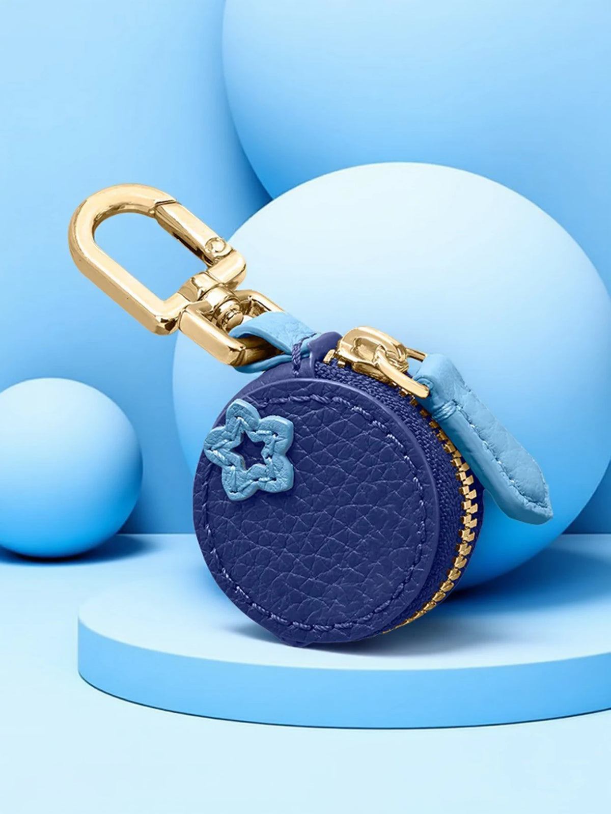 A purple coin purse keychain with a gold clasp and blue fabric, resting on light blue spherical props.