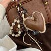 Brown leather heart pendant keychain with a long brown and white tassel attached to a tan leather bag.