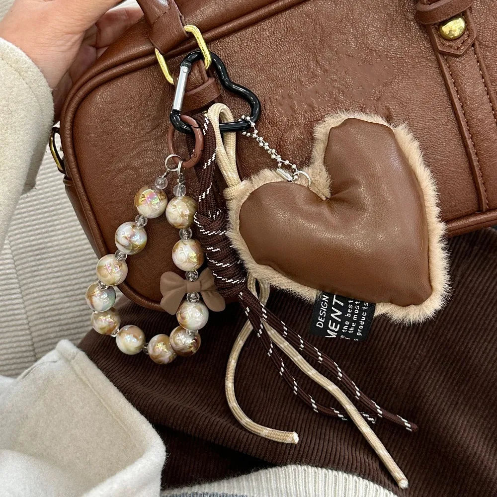 Brown leather heart pendant keychain with a long brown and white tassel attached to a tan leather bag.