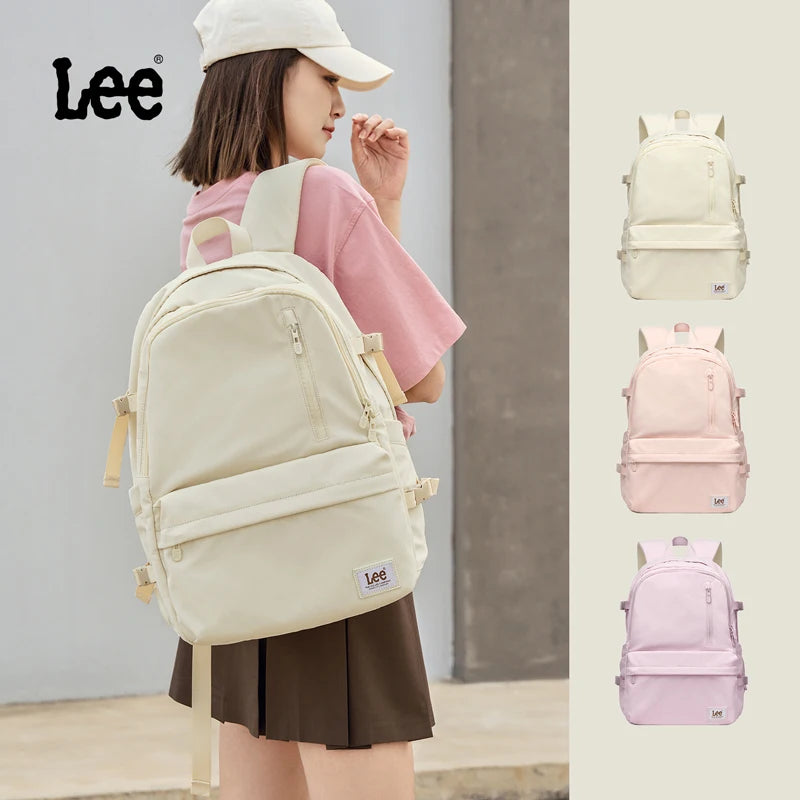 A young woman is wearing a beige Oxford school backpack from Lee, shown alongside pink and purple color variations.