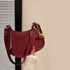 A maroon PU leather shoulder bag with a gold chain and cherry pendant is being held against a light wall.