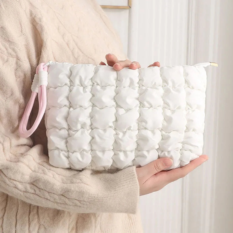 A white quilted puffer makeup bag is held by a person wearing a beige sweater.