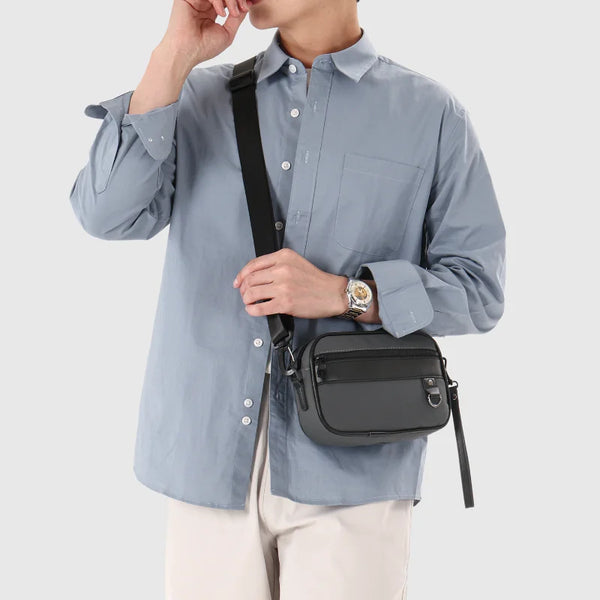 A woman wearing a light blue shirt and beige pants holds a black PU leather crossbody bag.
