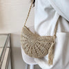 A light beige handmade rattan straw crossbody bag hanging from a white blazer sleeve.