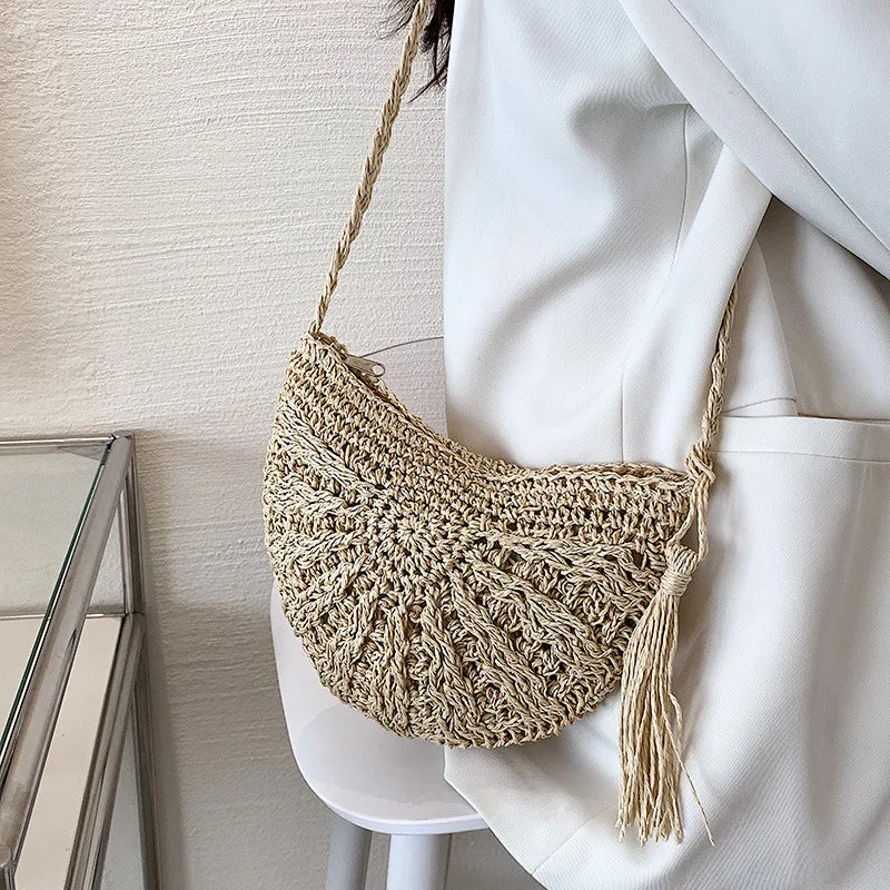 A light beige handmade rattan straw crossbody bag hanging from a white blazer sleeve.
