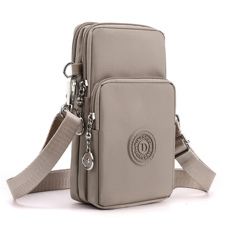 A light beige compact nylon crossbody phone bag with a leather strap and circular emblem.