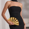A woman wearing a black strapless dress holds a gold acrylic chain crossbody bag.