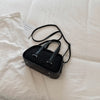 Black leather mini crossbody bag with textured crocodile pattern resting on a white fabric background.