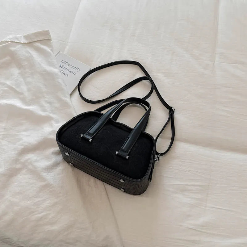Black leather mini crossbody bag with textured crocodile pattern resting on a white fabric background.