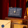 A dark blue leather square folding wallet with gold accents rests on a wooden surface next to a vintage radio.
