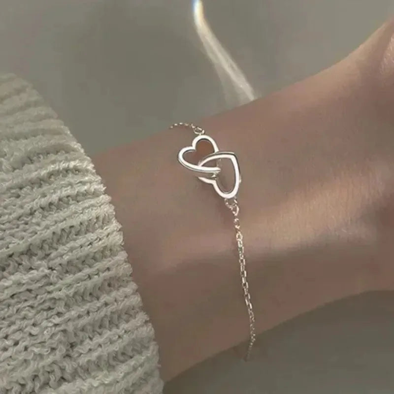 A close-up of a wrist wearing a delicate silver heart charm bracelet with a portrait pendant.