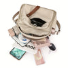 A beige multi-pocket shoulder crossbody bag with brown leather accents and various small items displayed around it.