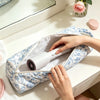 A person is placing a white hair dryer into a blue and white quilted storage bag on a white table.
