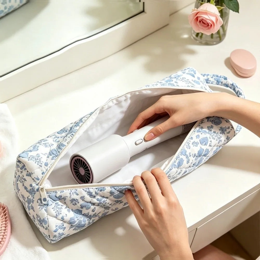 A person is placing a white hair dryer into a blue and white quilted storage bag on a white table.