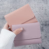 A hand holds a pink slim multi-functional card wallet for students with a white knitted sleeve in a gray background.