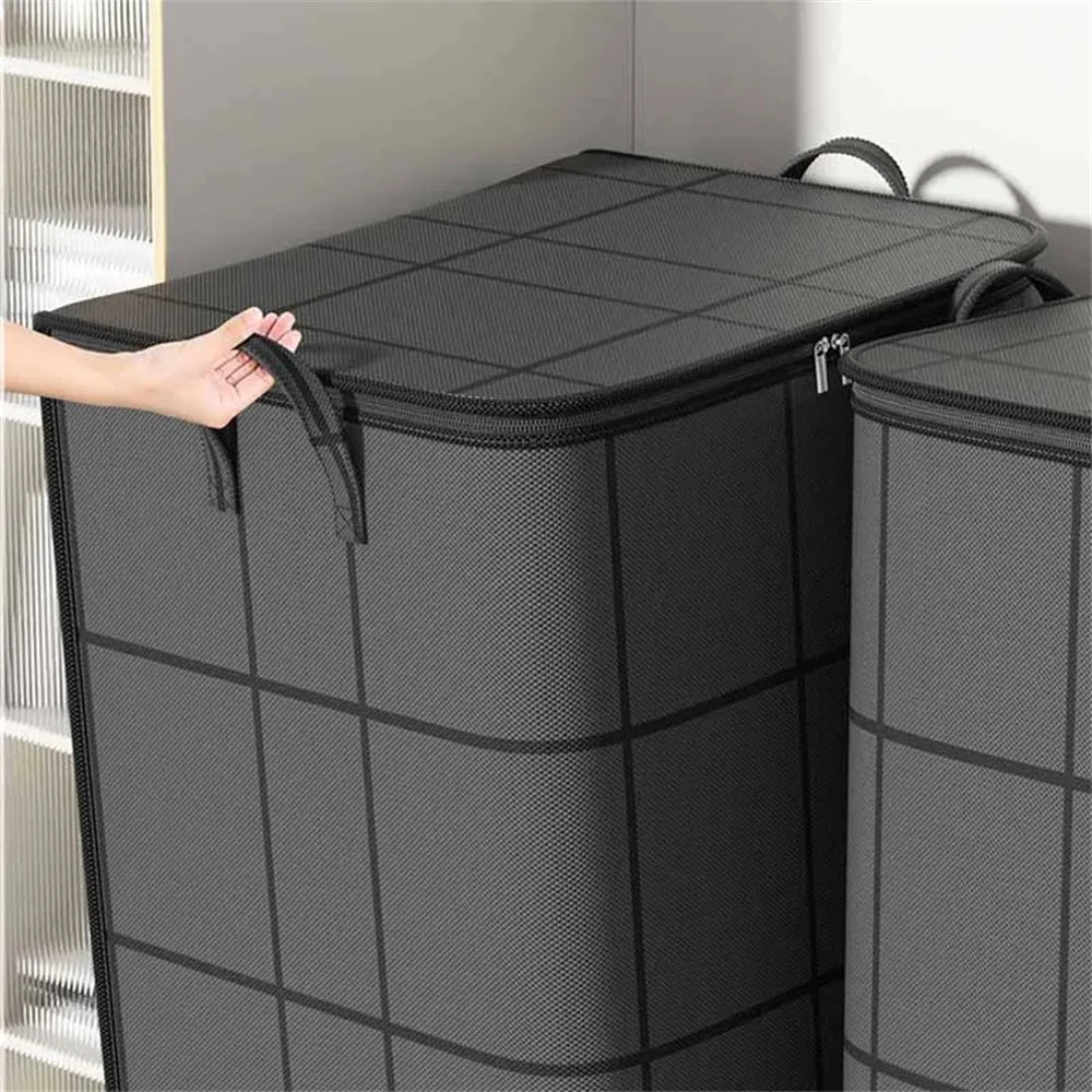 A hand is lifting a large black foldable non-woven storage bag, showing its textured surface and handle.