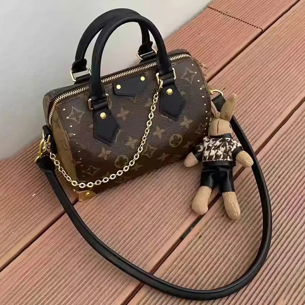 A brown cowhide leather handbag with a black strap and a small stuffed animal attached, resting on a wooden surface.