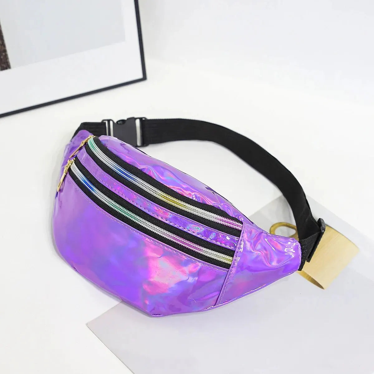 A purple holographic sequin waist bag with black adjustable strap resting on a white surface.