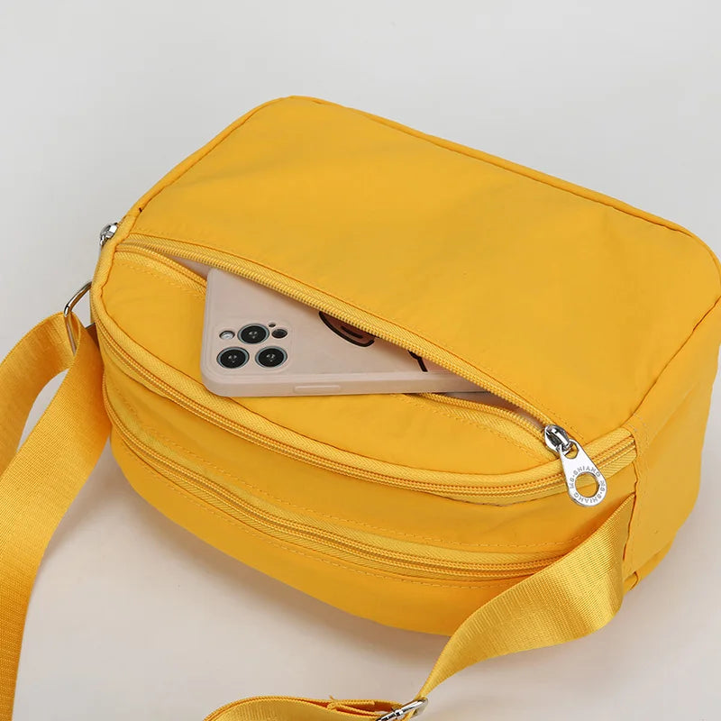 Gelbe Nylon-Crossbody-Tasche mit Reißverschluss, die ein Smartphone zeigt.