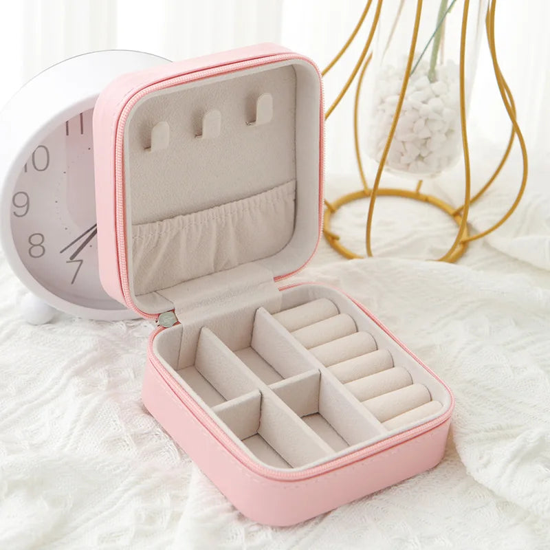 A pink compact leather jewelry travel box with an open lid and interior compartments resting on a white surface.