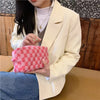 A person holds a pink and white checkered makeup bag set in front of a light beige blazer.