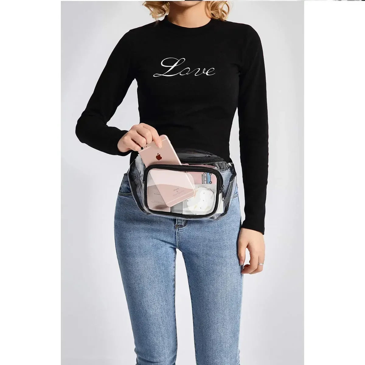 A woman wearing a black long-sleeve shirt and jeans holds a clear waterproof transparent fanny pack.