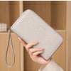 A close-up of a slim beige PU leather wallet with a zipper closure is shown being held by a hand.