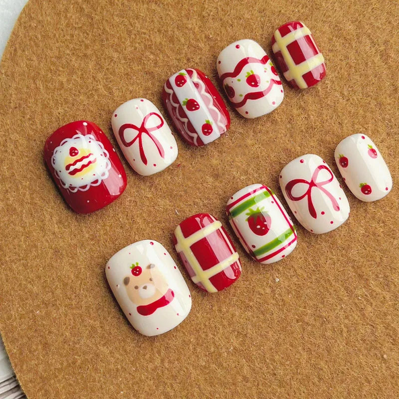 A set of cute cartoon press-on nails in red and white with various designs like Christmas and fruit on a brown surface.