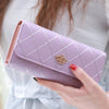 A hand holds a light purple quilted wallet with a gold crown buckle against a white and blue striped background.