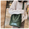 A woman holds a dark green alligator pattern leather crossbody bag against a light beige sweater.