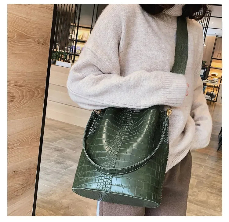 A woman holds a dark green alligator pattern leather crossbody bag against a light beige sweater.