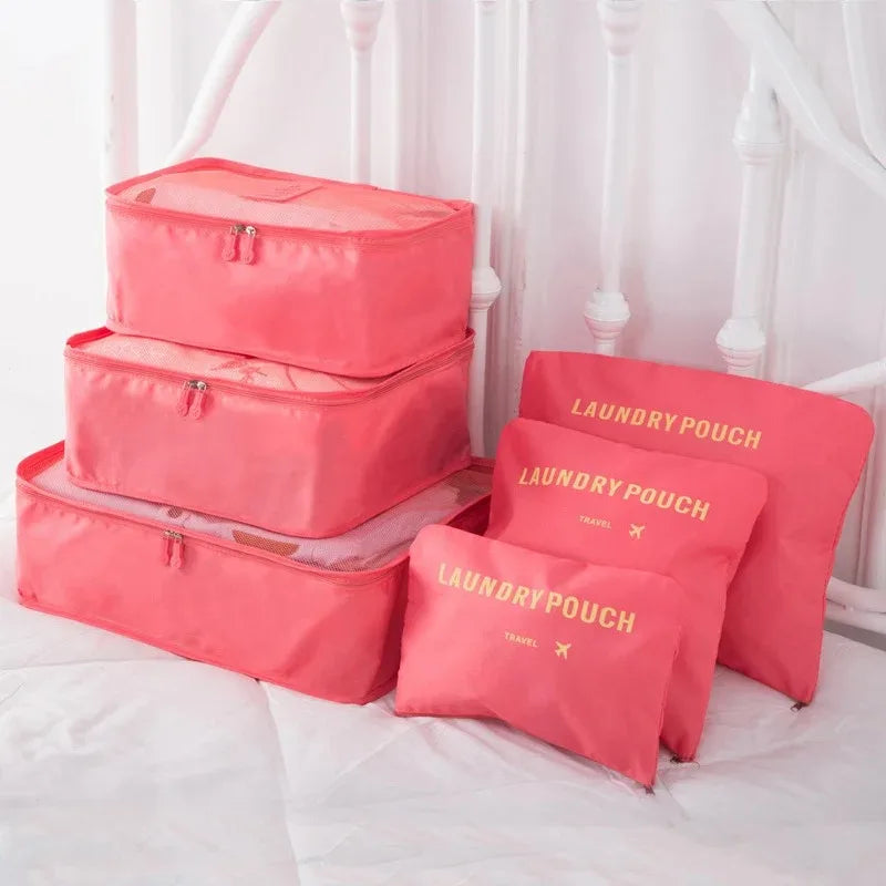 A set of pink laundry pouches and packing cubes for travel organization displayed on a white bed.