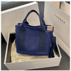 A navy blue canvas crossbody bag with a padded strap is displayed in a white box.
