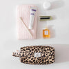 A leopard print large capacity waterproof travel makeup organizer bag with a small brush and bottle on a white surface.