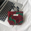 A deep green fabric pouch with red floral embroidery rests on a white laptop.