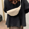 A woman wearing a black sweater and brown pants holds a beige nylon crossbody sling bag.