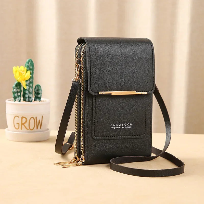 A black women's touch screen crossbody shoulder bag with gold hardware resting on a light surface.