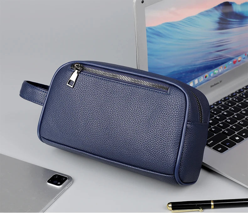 Pochette de soirée en cuir PU bleu marine avec fermeture éclair et sangle posée sur un ordinateur portable argenté.