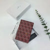 A geometric print passport wallet in a maroon pattern is displayed inside its white box.
