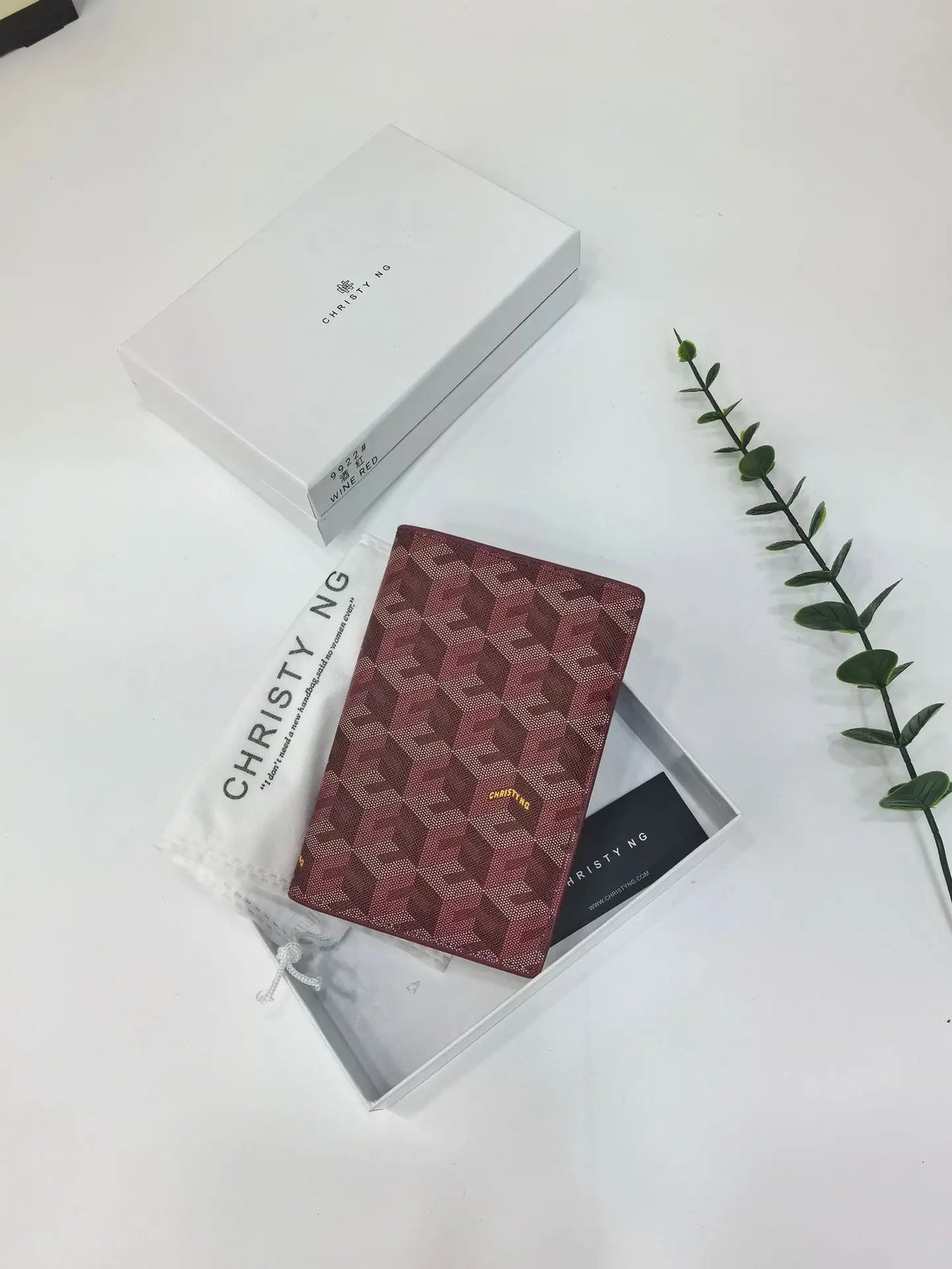 A geometric print passport wallet in a maroon pattern is displayed inside its white box.