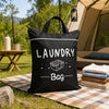 Black canvas laundry bag with a handle resting on a checkered mat outdoors near a tent.