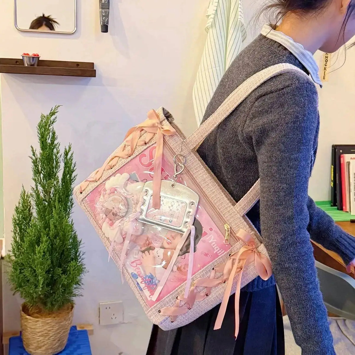 A person is holding a pink and white transparent shoulder tote bag with floral accents against a white wall.