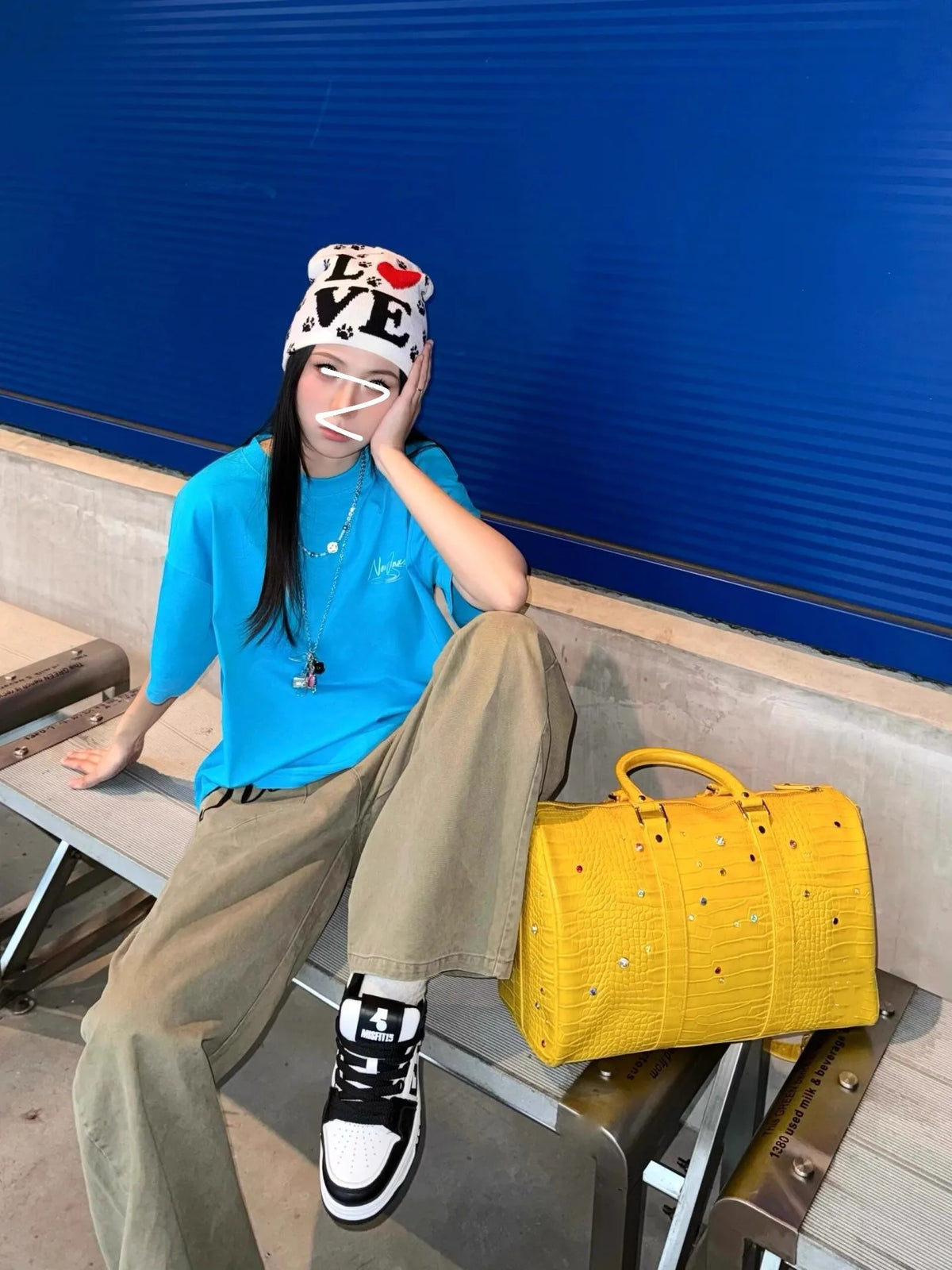 A person wearing a blue shirt and tan pants is sitting on a ledge next to a yellow faux crocodile tote bag.