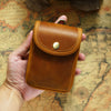 A brown leather men's multi-functional waist bag is held in a hand against an old map background.