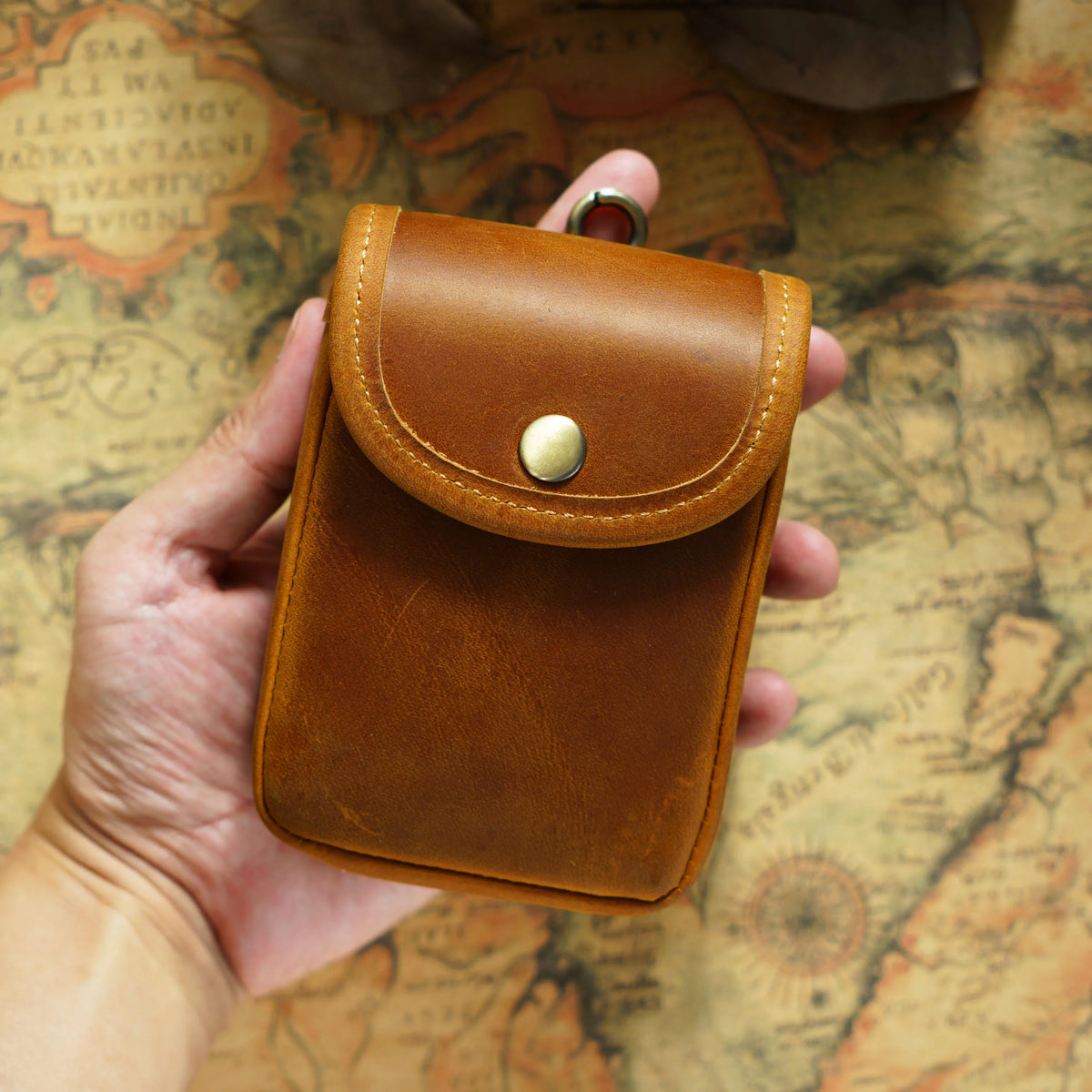A brown leather men's multi-functional waist bag is held in a hand against an old map background.