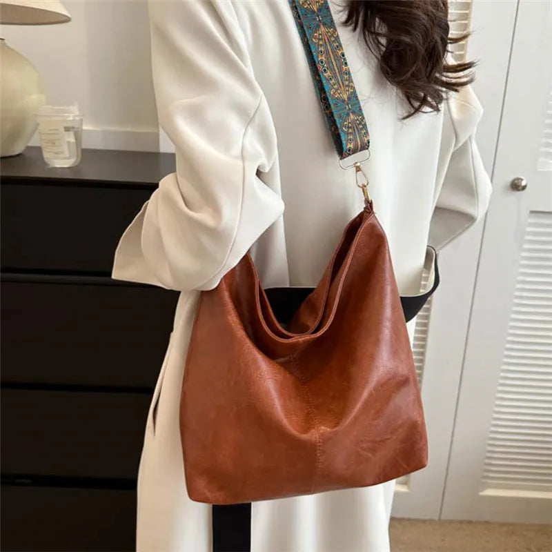 A close-up of a tan leather shoulder bag with an embroidered strap hanging from a white blazer.
