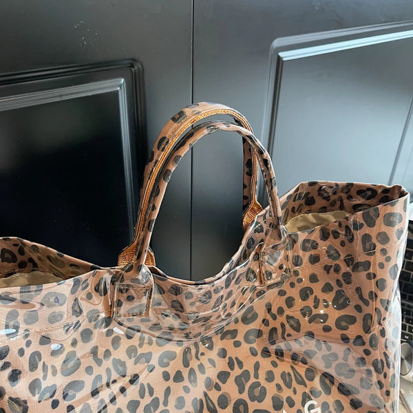 A clear plastic tote bag with a leopard print pattern is shown against a dark background.