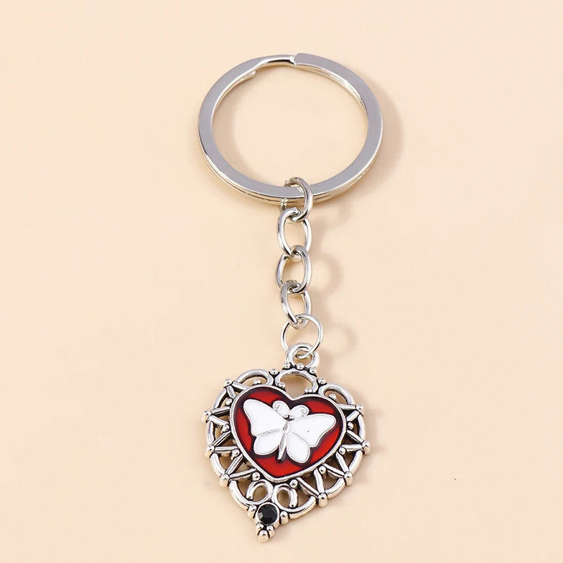 Silver heart-shaped keychain featuring a white butterfly pendant with red accents and intricate metalwork