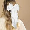 A woman with long blonde hair is shown from the back wearing a white silk bow hair clip.